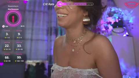 Media: Video of a smiling, light-skinned woman with curly hair, wearing a white, strapless lace dress and large silver earrings, set against a purple-lit indoor background.