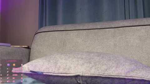 Video of a gray, textured sofa with a cushion, featuring a \"Game of Thrones\" magazine cover. The background includes a blue curtain and a soft, ambient purple light.