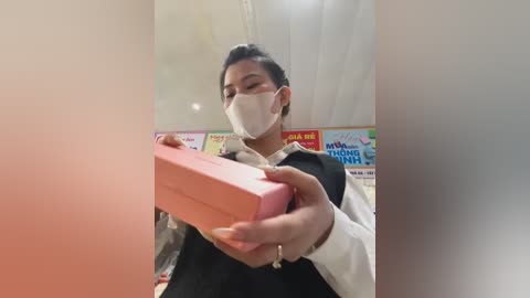 Media: Video of an Asian man in a mask, black vest, white shirt, holding a pink gift box, surrounded by colorful Vietnamese signage.