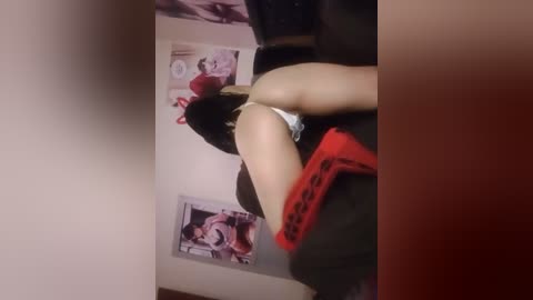 Media: A video captures a woman with light skin, black hair, and a red dress, leaning over a dark couch. A black and white poster of Marilyn Monroe is on the wall behind her.