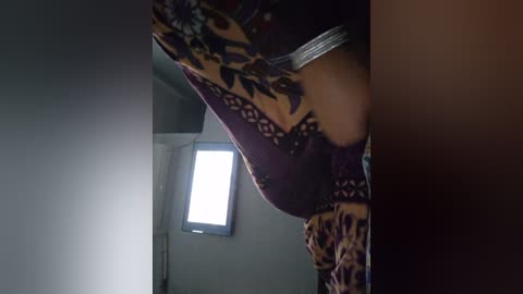 Media: Video of a woman in a dark room, wearing a patterned, maroon dress, bending over to adjust a TV. The background is dimly lit with a window.