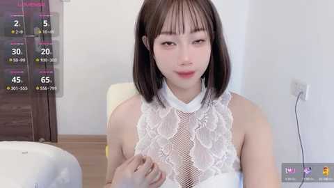 Media: A video of an East Asian woman with straight black hair and fair skin, wearing a white lace top, sitting indoors.