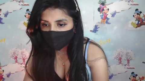 Media: A video of a woman with long black hair, wearing a black face mask, a black tank top, and a light blue bra, standing against a background with Disney characters.