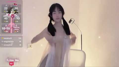 Media: A candid video of an East Asian woman with long black pigtails, partially covering her breasts with a white cloth, standing in a dimly lit room.