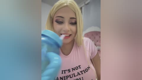 Media: Video of a young, blonde woman with fair skin, wearing a pink t-shirt with \"IT'S NOT AN EXERCISE\" text, brushing her teeth with a blue toothbrush in a modern bathroom.