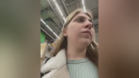 Media: Video of a young Caucasian woman with long blonde hair, wearing a light blue sweater, standing in an airport terminal with a stuffed animal in her hand.