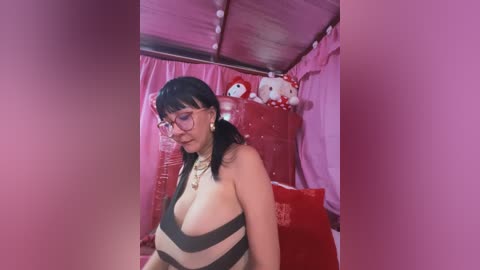 Media: Video of a plus-size Asian woman with dark hair, glasses, and a black-and-white striped halter top, posing in a pink room with stuffed toys.