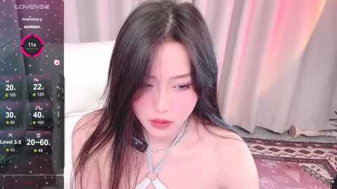 Media: Video of a young Asian woman with long black hair, wearing a white strapless dress, in a soft-lit room with pink curtains.