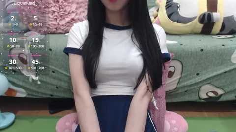 Media: A video of an Asian woman with long black hair and fair skin, wearing a white and navy blue athletic outfit, sitting on a pink cushioned chair in a colorful room.