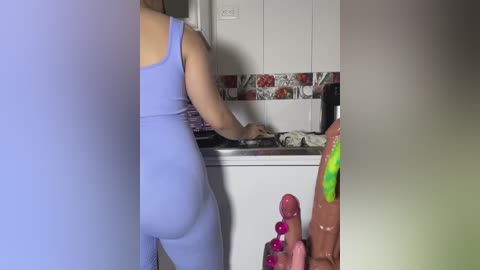 Media: Video of a light-skinned woman in a tight, purple sports bra and leggings, cooking in a modern kitchen with white cabinets and red floral backsplash.