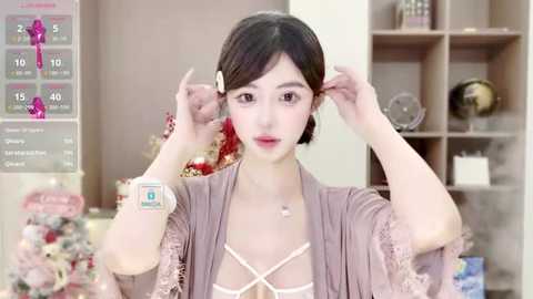 Media: A video of a young Asian woman with short black hair, wearing a light gray, lace-trimmed top, adjusting her hair in a modern living room.