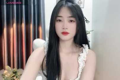 Media: Video of an Asian woman with long black hair, fair skin, and red lipstick, wearing a white lace top, against a backdrop of metallic curtains and white walls.