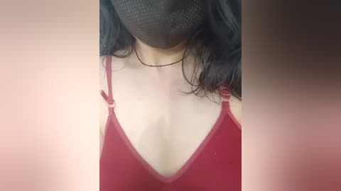 Media: Video of a woman with fair skin, wearing a red, low-cut spaghetti-strap top, black face mask, and long, wavy black hair.