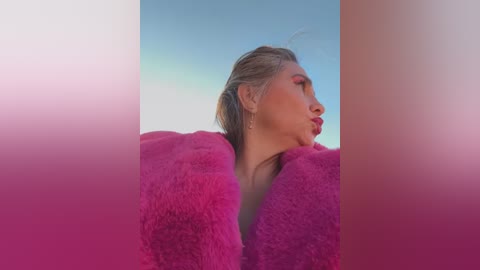 Media: A video of a woman with light skin, styled blonde hair, wearing a pink fuzzy coat against a clear blue sky. Her makeup includes pink eyeshadow and red lipstick.