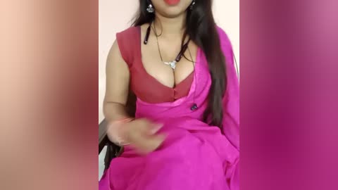 Media: A video of a South Asian woman with medium skin tone, wearing a deep pink sari with a red blouse, showing cleavage, against a gradient pink background.