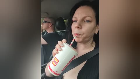 Media: Video of a woman with long black hair, wearing a black top, drinking a Starbucks Frappuccino through a straw while seated in a car.