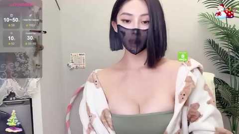 Media: Video of a woman with medium skin tone, straight black hair, wearing a green bra and a sheer black mask, standing indoors, surrounded by digital health data screens and a green plant.