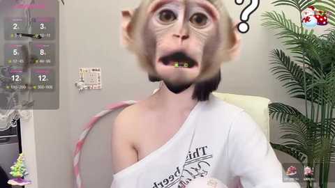 Media: A digital video of a startled-looking woman with a monkey head, wearing a white t-shirt, in a doctor's office with a calendar and plant in the background.