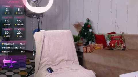 Media: Video of a cozy living room with a beige armchair, a lit Christmas tree, wrapped presents, and a glowing ring light, displaying social media stats in the background.