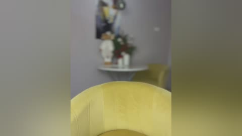 Media: A blurry video of a modern interior featuring a yellow armchair, a white round table, and a framed painting on a lavender wall, with a vase of flowers in the background.