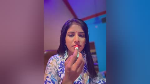 Media: Video of a young Latina woman with long black hair, wearing a white floral blouse, brushing her teeth. She is in a bathroom with blue and pink lighting.