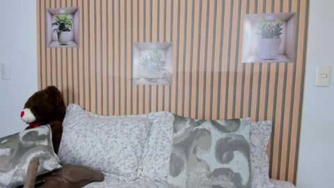 Media: Video of a cozy bedroom featuring a plush brown teddy bear, light blue and gray elephant-patterned bedding, and a wooden headboard with three inset plant holders.