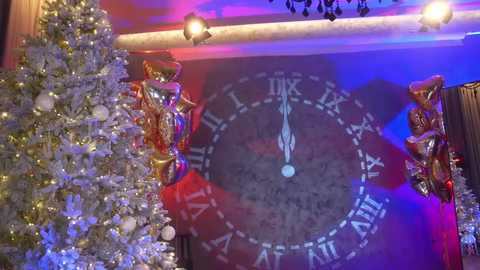 Media: Video of a festive room with a decorated Christmas tree on the left, a glowing blue and purple clock with Roman numerals on the wall, and golden and red festive decor.