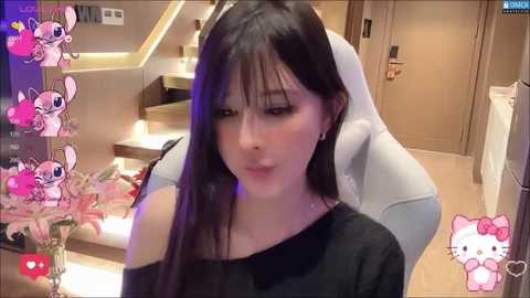 Media: A video of a young Asian woman with long black hair, wearing a black off-shoulder top, sitting in a modern, well-lit room with a staircase and plush furniture.