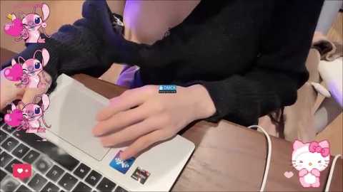 A video of a person in a black sweater, using a laptop, with virtual stickers of Stitch and Hello Kitty. The background is blurred, showing a beige bag.