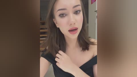 Media: Video of a fair-skinned, light-haired young woman with bold makeup, wearing a black off-shoulder top, captured in a blurred, dimly lit indoor setting.