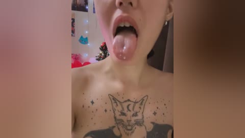 Media: Video of a young woman with light skin, topless, tongue out, licking her nipple, showing a tattoo of a fox on her chest. Background shows colorful Christmas decorations and fairy lights.