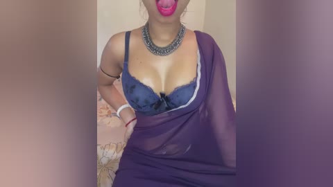 Media: Video of a curvy woman in a deep blue bra, purple sheer sarong, and silver necklace. She has her lips puckered, tongue out, in a suggestive pose.