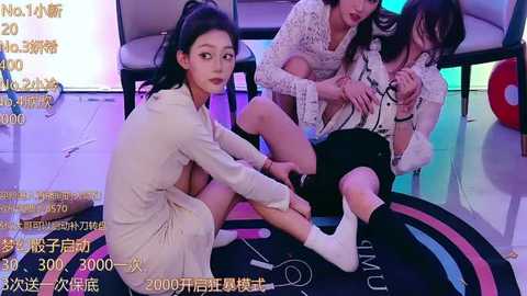 Media: Video of three Asian women in a studio, one kneeling, one sitting, and one standing, all with dark hair, wearing casual, patterned outfits, against a colorful backdrop.