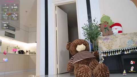 Media: Video of a plush teddy bear lying on the floor near a door in a modern, light-toned kitchen with a white refrigerator and potted plants.