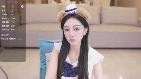 Media: Video of an Asian woman with long black hair and fair skin, wearing a sailor outfit with a white cap, sitting indoors on a beige carpet.