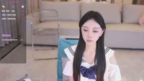 Media: Video of a young East Asian woman with long black hair, wearing a schoolgirl uniform, sitting on a couch in a modern living room.