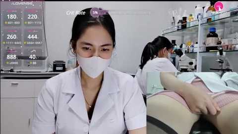 A video shows two Asian women in lab coats and masks working in a sterile lab. The foreground features a woman with dark hair, while the background has a woman bent over a table.