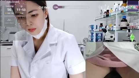 Video of an East Asian woman in a white lab coat and face mask, looking down, in a sterile lab setting.