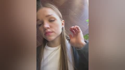 Video of a young Caucasian woman with fair skin, long straight blonde hair, and closed eyes, sitting indoors, possibly in a car, with a neutral expression.