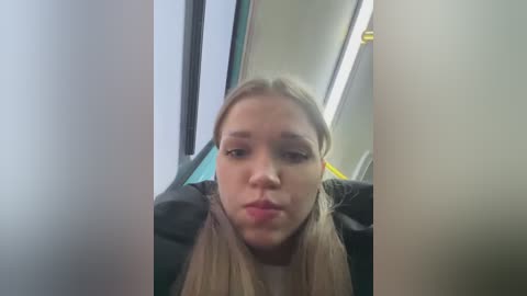 Media: A video of a young, blonde woman with fair skin, wearing a black jacket, sitting on a public bus. She has a neutral expression and is looking directly at the camera.