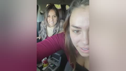 Media: Video of a woman in a maroon top, smiling and taking a selfie inside a car, with another woman in the background wearing a plaid shirt.