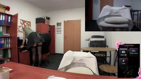 Media: A video of a woman in a green dress bending over, revealing her black stockings and thong. The background shows a cluttered office with a printer, books, and a desk. A close-up inset of her thong is included.