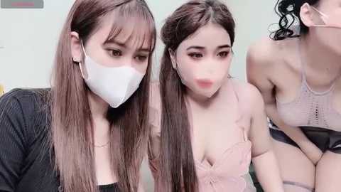 Media: Video of two young Asian women with long brown hair, wearing white face masks, black tops, and sitting close together.