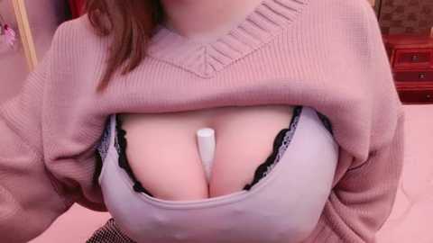 Media: Video of a light-skinned woman with medium-length brown hair, lifting a pink sweater to reveal a white bra with black lace trim and a large, round breast. Background includes pink walls and a red dresser.