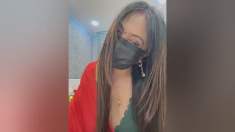 Media: Video of a young woman with long, straight brown hair, wearing a black face mask, red blouse, and green lace bra. Background shows a blue and white patterned wall.