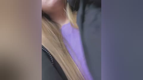 Video of a close-up of a person's neck and shoulder, showing light skin, long blonde hair, a purple shirt, and black jacket. The image is blurred, focusing on texture and color rather than details.