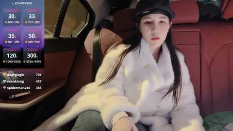 Media: A video shows an East Asian woman with long black hair, wearing a black beret and white fur coat, sitting in a red leather car seat.