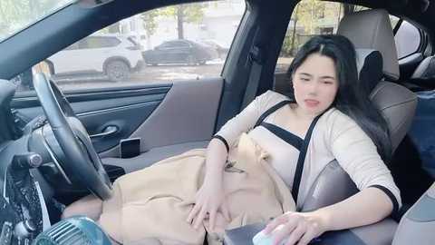 Media: Video of a woman with long black hair, wearing a beige skirt and white top, sleeping in the backseat of a car.