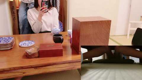 Media: Video of an Asian woman in a traditional kimono, holding a smartphone, reflected in a wooden table with Japanese tea set, pottery, and red box. Background shows tatami mats and sliding doors.