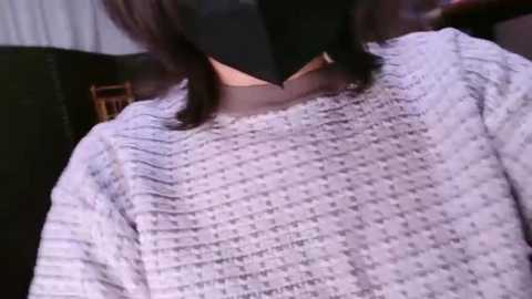 Media: Video of a person wearing a white, textured, knitted sweater with ribbed cuffs, partially visible face. Background features a dark-colored sofa and a white curtain.